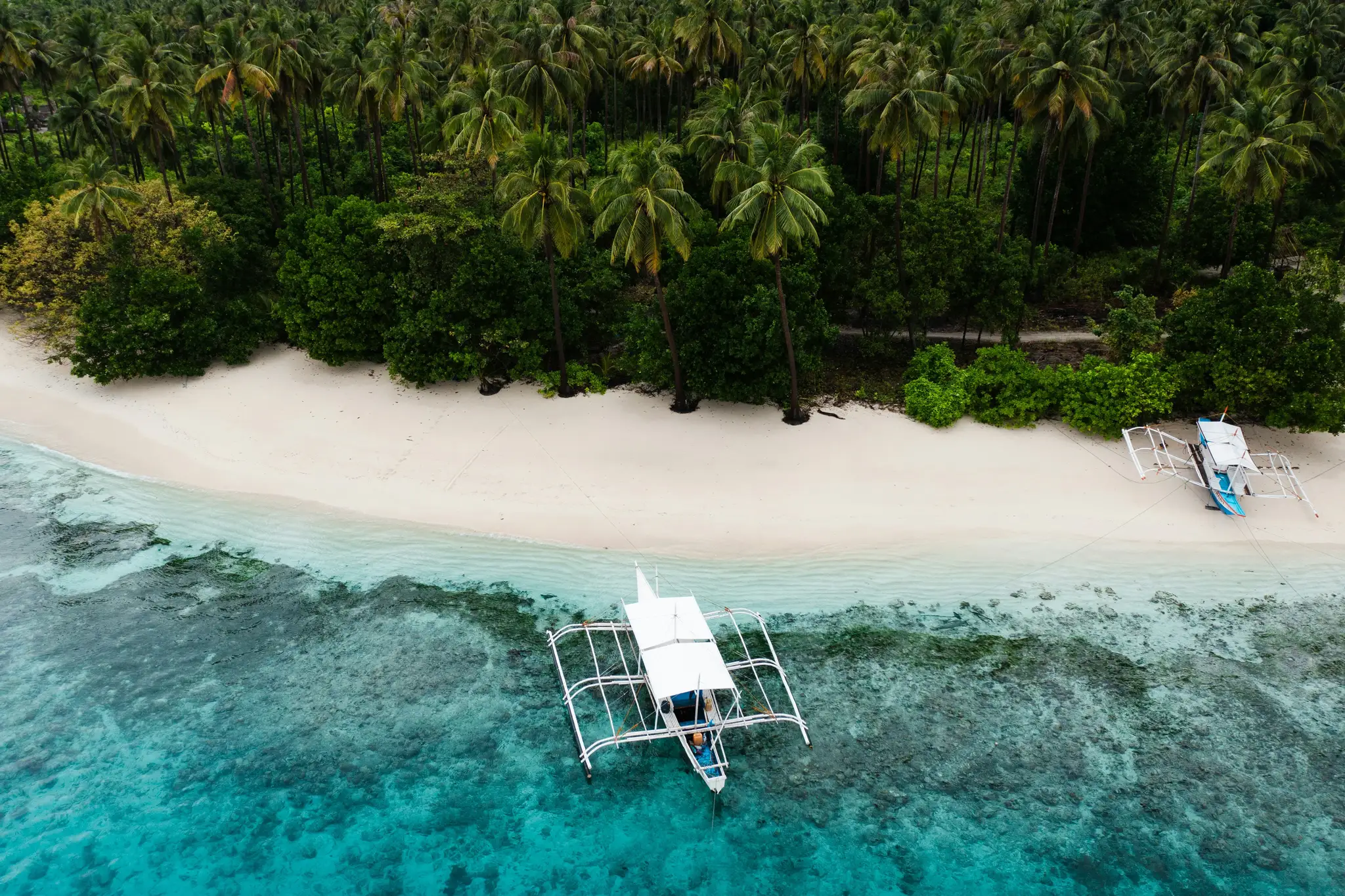 A boat moored off a white sand beach, seen from above