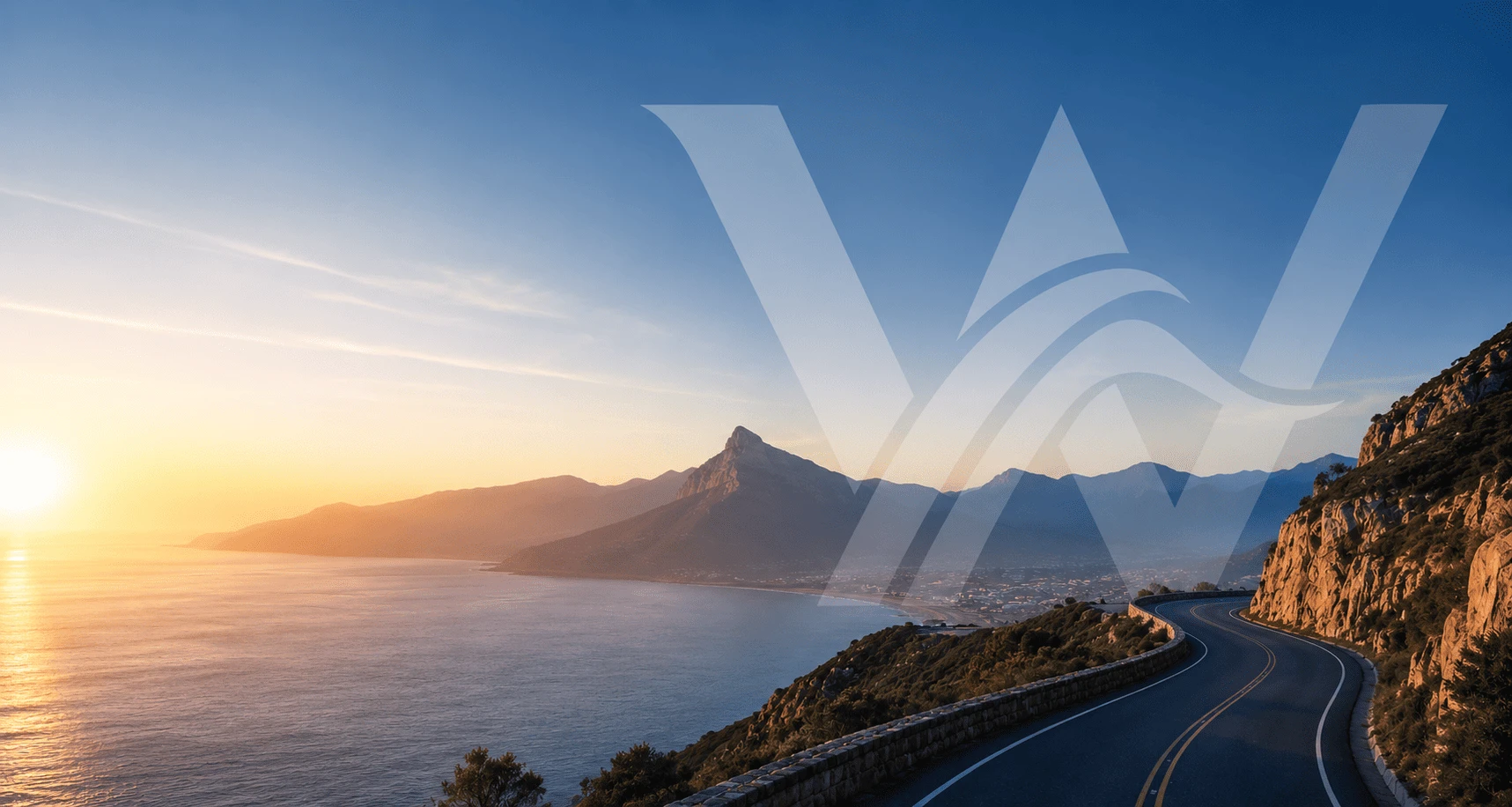 A coastal road curving along a mountainside above the sea at sunset